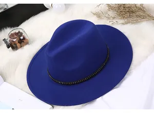 Detail of dark blue wool fedora hat with metal stud band on white faux fur background