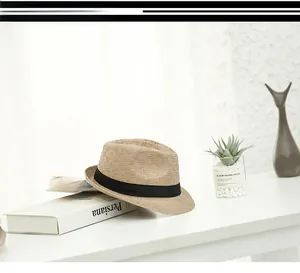 Close-up of a stylish straw fedora hat with a black ribbon band on a minimalist table