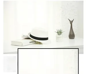 Close-up of white woven straw fedora hat with a classic black ribbon band on a desk