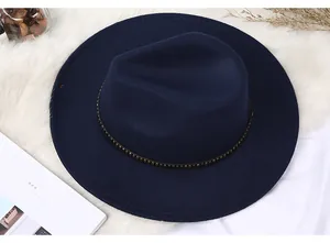 Detail of navy blue wool fedora hat with gold rivet band on white fur texture