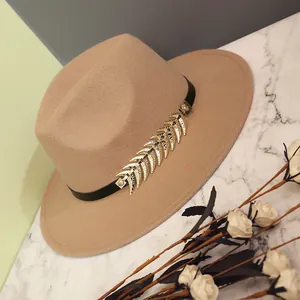 Elegant camel wool fedora hat with black band and golden metal leaf on marble surface