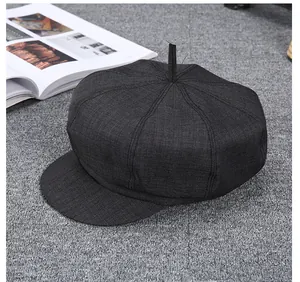 Detail view of a vintage dark grey wool newsboy hat on a neutral textured background