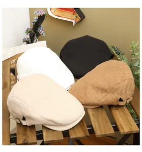 Detail view of four linen-textured flat caps with adjustable metal buckles on wooden bench