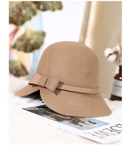 Detail of wool cloche hat with a bow and notched brim on a white plush background