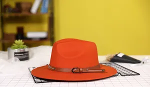 Detail of orange fedora with brown leather strap, metal buckle, and silver rivets