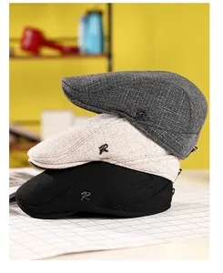 Gros plan de bérets en coton et lin empilés en gris, beige et noir avec logo R en métal