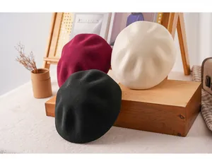Close-up of wool beret hats in black, burgundy and beige stacked on a rustic wooden tray