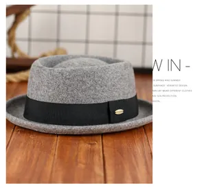 Détail d'un chapeau pork pie en laine avec ruban noir et plaque dorée sur feutre gris