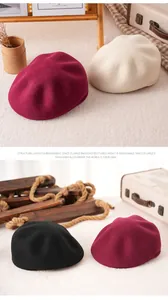 Close-up of wool beret hats in burgundy, beige, and black with a soft texture