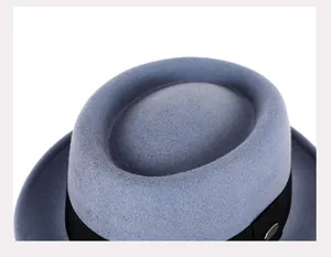 Gros plan d'un chapeau Pork Pie en laine bleu-gris avec ruban noir et logo en métal