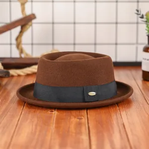 Chapeau pork pie élégant en laine marron avec ruban noir et badge doré sur bureau en bois