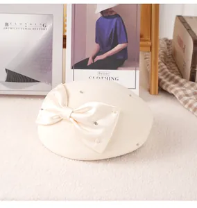 Detail of a creamy white wool beret with silk bow, pearls, and crystals on fuzzy background