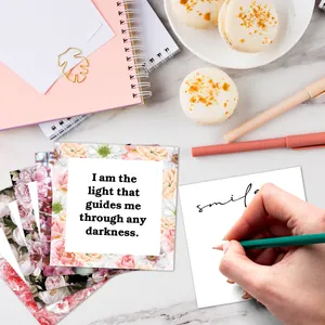 Flat lay of floral affirmation cards with inspirational quotes on white marble surface