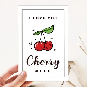 Détail d'une carte de remerciement cerise tenue à la main avec texte I LOVE YOU Cherry MUCH