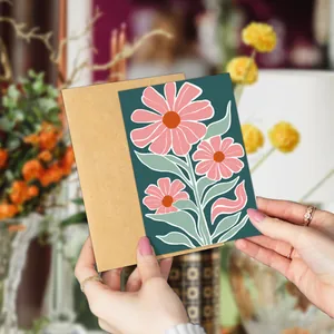 Close-up of hand holding floral thank you card with abstract daisies and kraft envelope