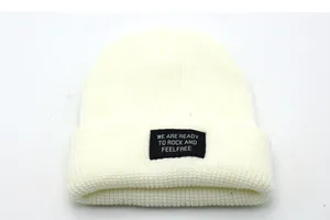 Detail of cream knit beanie featuring thick texture and embroidered letter patch