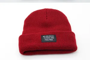 Close-up of dark red ribbed knit beanie featuring a black text patch and soft texture