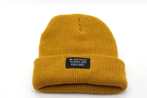Close-up of a yellow ribbed knit beanie featuring a black woven patch with white lettering