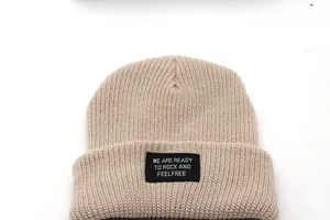 Detail of beige ribbed knit beanie featuring a square black lettered fabric patch