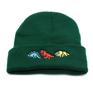Close-up of three colorful embroidered dinosaurs on a dark green knit beanie
