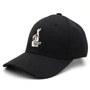 Détail de la broderie TRUST ME et du geste des doigts croisés sur une casquette noire