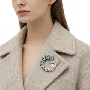 Close-up of sparkling blue crystal wreath brooch with white pearl on camel wool coat