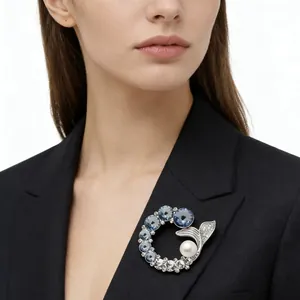Elegant fishtail brooch featuring blue crystals and a pearl on a black blazer