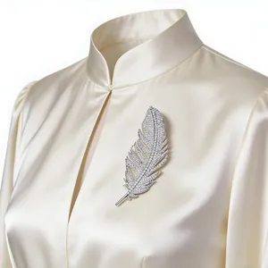Detail of silver feather brooch with full pavé crystals on a white silk blouse