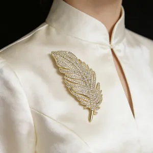 Close-up of a sparkling gold feather brooch with crystals pinned on a white satin dress