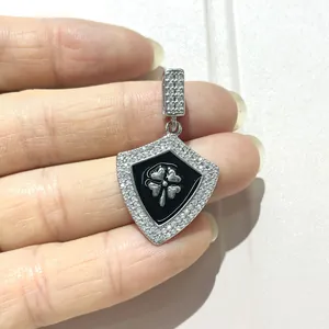 Macro shot of silver shield pendant with black enamel, zircon stones and clover motif
