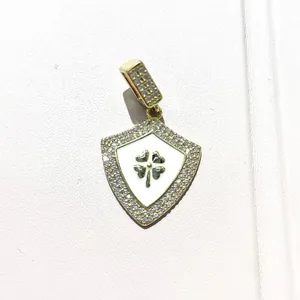 Macro view of gold shield pendant with white enamel clover and pavé zircon details