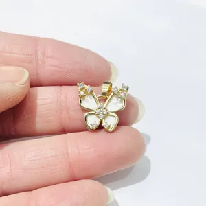 Detailed close-up of a gold-plated butterfly pendant with white enamel and sparkling crystals