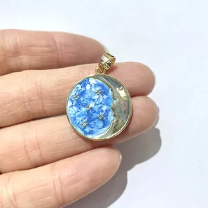 Golden round pendant with blue enamel starry sky and moon detail held in hand