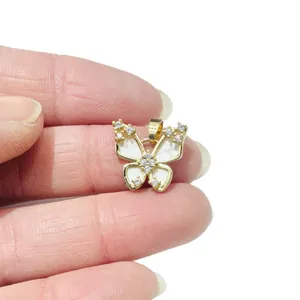 Golden butterfly pendant with white enamel and sparkling zircons held by hand
