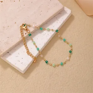 Elegant gold chain bracelet with green and white square glass beads on textured stone