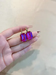 Detailed close-up of a rectangular magenta crystal earring with a gold metal finish