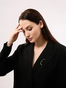 Dettaglio di una spilla minimalista argentata a forma di viso sul risvolto di un blazer nero