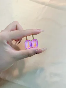 Detail of square colorful zircon earrings with pinkish-purple iridescent stones in gold claws