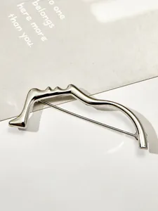 Dettaglio di una spilla minimalista in argento con silhouette di viso astratta lucida