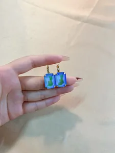 Detail of square colorful zircon earrings with gold lever-back hooks and blue-green gems
