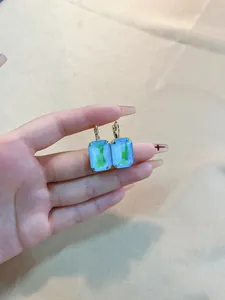 Detail of gold earrings with rectangular mint green crystals on champagne silk background