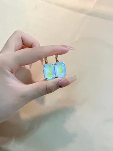 Macro view of gold hoop earrings featuring large rectangle light blue iridescent crystals
