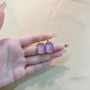 Golden earrings with square iridescent rainbow stones shown on a warm textile background
