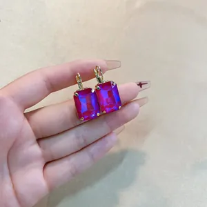 Golden earrings with large rectangular purple zircon and leverback closure held by hand