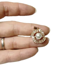 Luxurious gold floral pearl pendant with baguette cubic zirconia, held for size reference