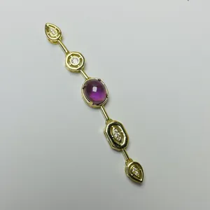 Detailed view of a gold pendant with a purple oval gemstone and white crystal accents