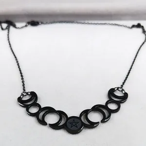 Close-up of black moon phase necklace with pentagram pendant on grey velvet