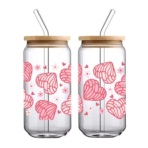 Detail of two can-shaped glasses with pink heart concha patterns, bamboo lids and straws