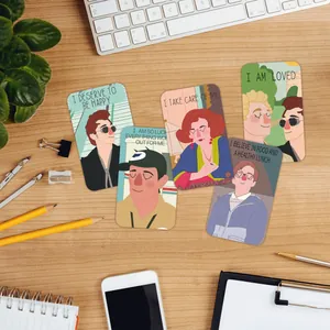 Close-up of colorful Good Omens affirmation cards on a wooden desk with office stationery