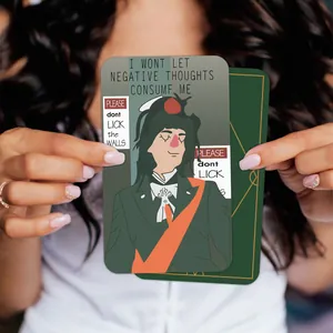 Hand holding Good Omens affirmation cards with illustrated cartoon figure and motivational quote
